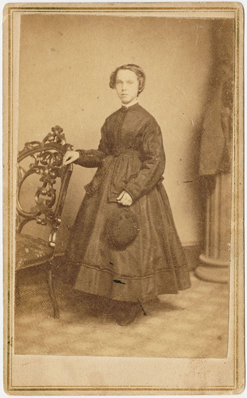 Young woman standing for a portrait with one arm resting on a decorative chair