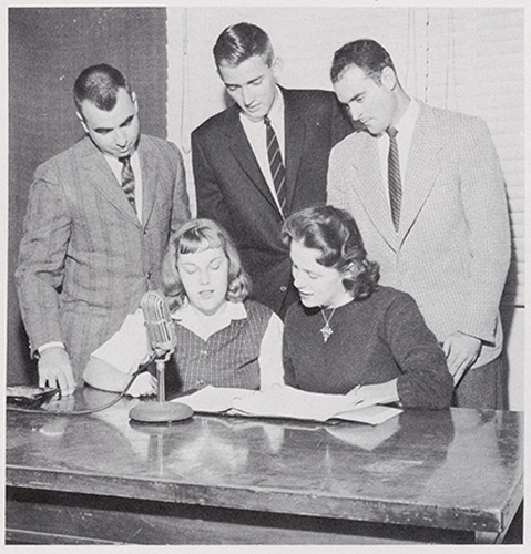 Group of students going live on-air, gathered around a microphone.