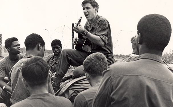 A servicemember plays acoustic guitar and sings in a crowd of others
