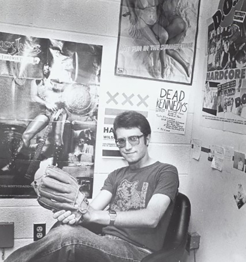 Jeff Krulik of WMUC sits with a baseball glove in a room with music posters on the walls.