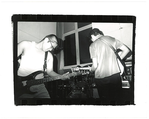 A poster with a black and white fisheye-lens photo of a drumset and other instruments in a recording studio, the photo is processed to be mostly blue and black and there is bold elongated yellow text.