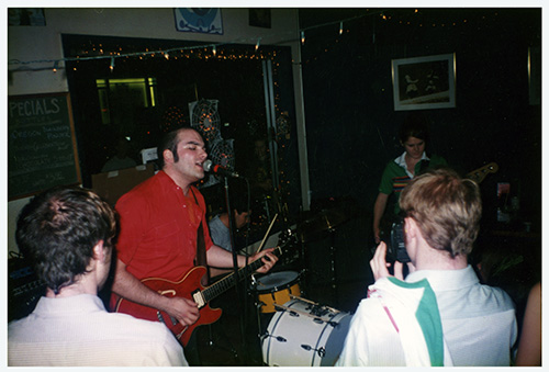 A poster with a black and white fisheye-lens photo of a drumset and other instruments in a recording studio, the photo is processed to be mostly blue and black and there is bold elongated yellow text.