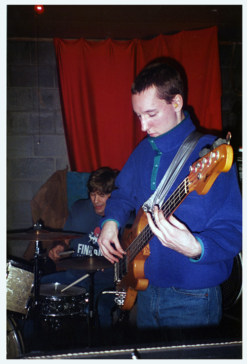 A poster with a black and white fisheye-lens photo of a drumset and other instruments in a recording studio, the photo is processed to be mostly blue and black and there is bold elongated yellow text.